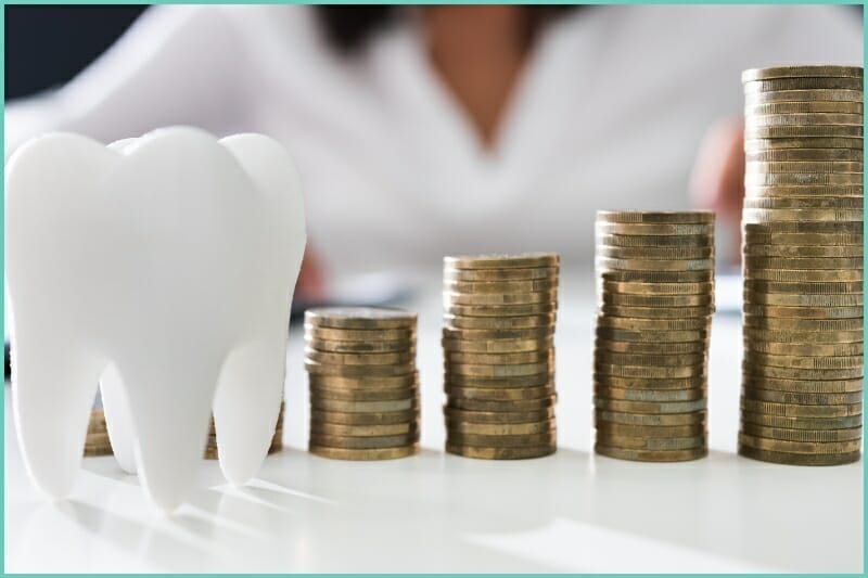 a big fake white tooth next to stacks of coins
