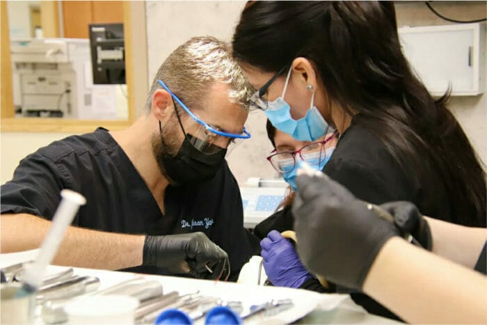 Dental surgeon and assistant performing an oral surgery procedure using specialized tools under bright clinical lighting.