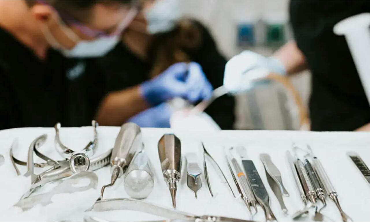 Close-up view of sterilized dental instruments arranged on a tray in a surgical setting with dentists working in the background.