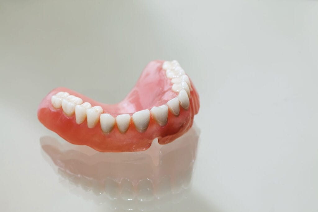 A lower denture set with artificial teeth resting on a reflective surface.