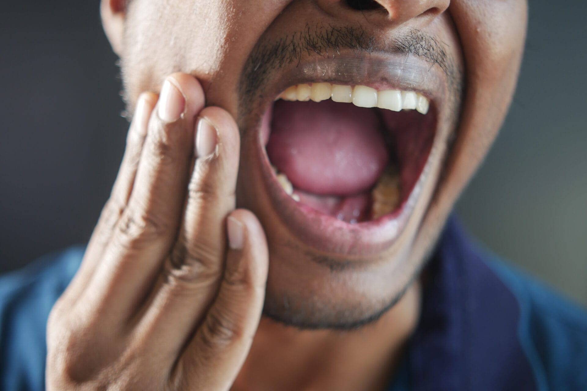 Man touching his jaw in pain, indicating discomfort or toothache.