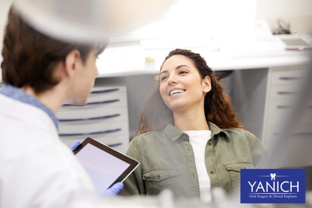 Smiling patient sitting in dental chair having a consultation with dentist about treatment options using a digital tablet.