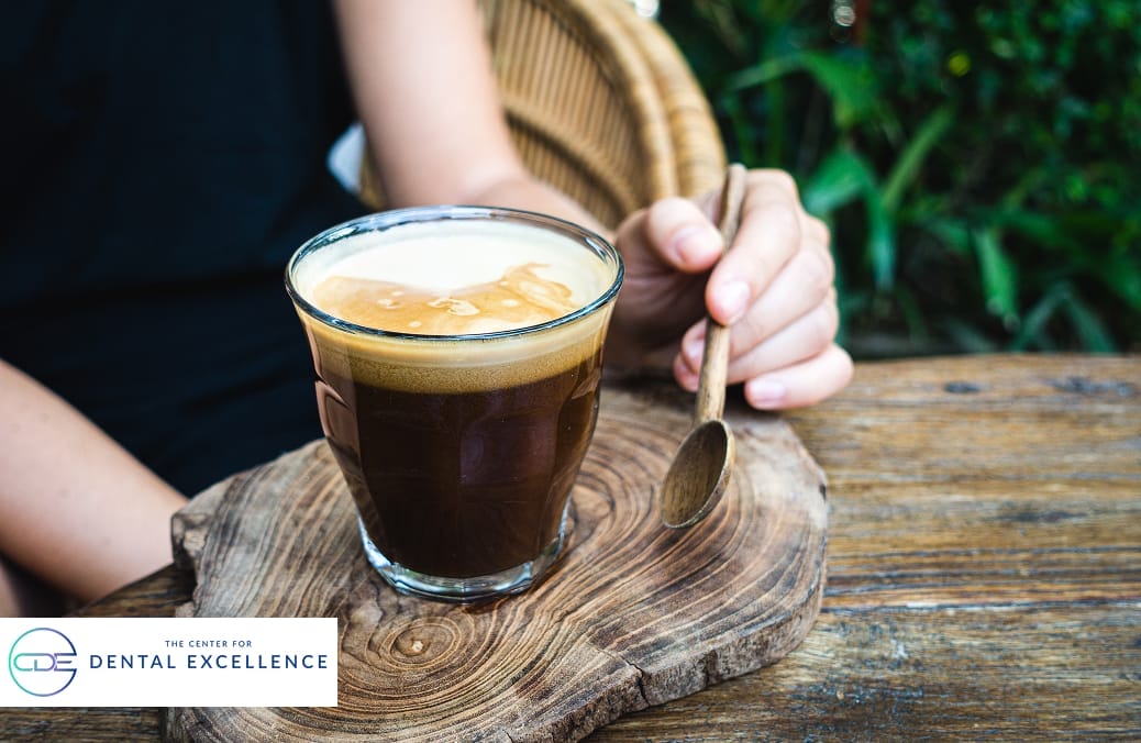 A person holding a cup of espresso coffee on a wooden table, illustrating habits that may affect dental enamel and teeth color.