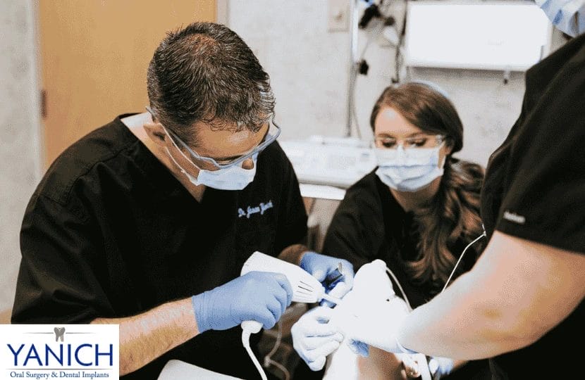 Dentist performing an oral surgery procedure with assistants, demonstrating precision and teamwork in a sterile environment.